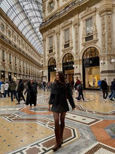 a woman is walking through the middle of an indoor shopping mall with lots of people