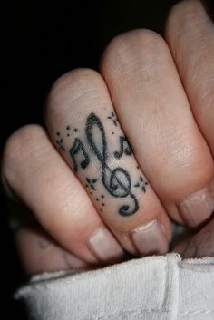 a person's hand with a musical note tattoo on their thumb and ring finger