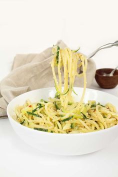 a white bowl filled with noodles and vegetables being held up by a fork over it