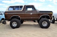 a brown truck parked in the sand with other trucks behind it and blue sky above