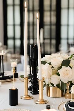 a table topped with white flowers and candles next to black plates on top of a table