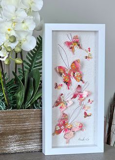 a white frame with pink and yellow butterflies on it next to a potted plant