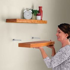 a woman holding a wooden shelf with two shelves above her head and an alarm clock on the wall