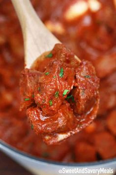 a wooden spoon full of meatballs and sauce with parsley on top in a pot