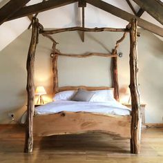 a bed made out of branches in a room with wooden floors and ceiling beams, along with two lamps on either side of the bed