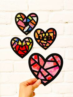 hand holding up stained glass hearts against a brick wall