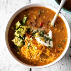 a bowl of soup with tortilla chips and avocado on the side