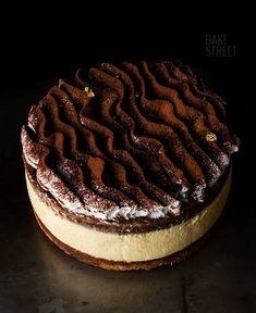 a chocolate cake with white frosting on a black tableclothed surface, in front of a dark background