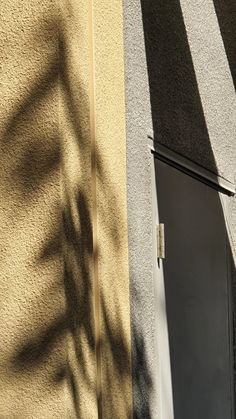 an open door on the side of a building next to a shadow of a tree