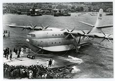 an old airplane is on the water with people standing around it and in front of it