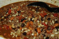 a white bowl filled with meat and beans next to a black spoon on top of a table