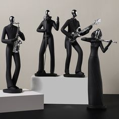 three black figurines playing musical instruments on white pedestals