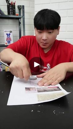 a young man sitting at a table cutting paper