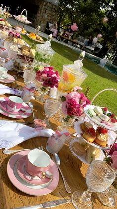 a long table is set with pink and white plates, cups, and desserts