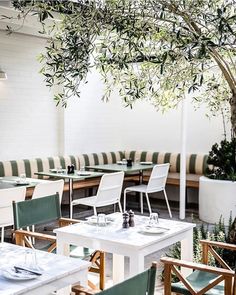 an outdoor dining area with tables, chairs and plants on the wall above them is white brick walls that are lined with green striped upholves