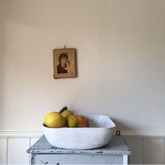 a white bowl filled with fruit sitting on top of a table next to a painting