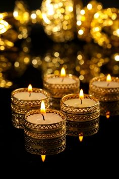 four lit candles sitting on top of a black table next to gold foiled decorations