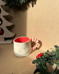 a white and red mug sitting on top of a table next to a christmas tree