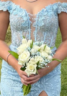 a woman in a blue dress holding a bouquet of white roses and greenery on the grass