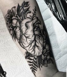 a black and white heart tattoo with flowers on the side of the arm, in front of a woman's leg