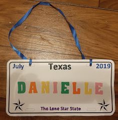 a sign that says danielle on it hanging from a wooden floor with a blue ribbon