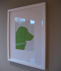 a white frame with a green silhouette of a dog on the wall next to it