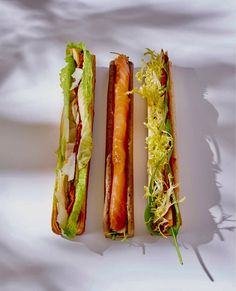 two sandwiches with lettuce, tomato and meat are on a white surface next to each other