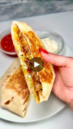 a person holding a burrito on a plate with sauces and ketchup