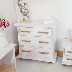 a giraffe statue sitting on top of a white dresser next to a vase with flowers