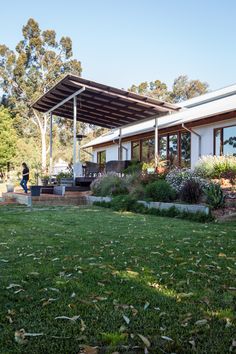 a house that is in the grass with some plants around it and a person standing outside