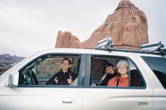 two women sitting in the passenger seat of a white car with mountains in the background