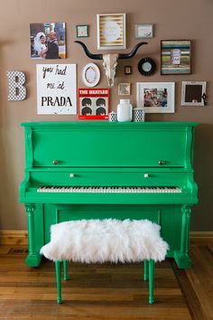 a green piano in front of a wall with pictures on it and a sheepskin footstool