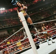 a woman standing on top of a white pole next to a wrestling ring in front of an audience