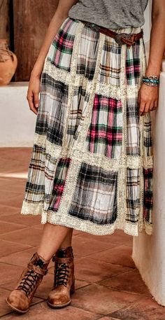 a woman standing next to a white pillar wearing a skirt with plaid print on it