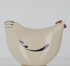 a white ceramic chicken bowl with black lines on it's face and nose, sitting on a table