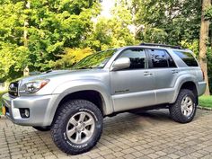 a silver toyota suv parked on top of a brick road in front of some trees