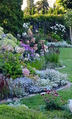 a garden filled with lots of different types of flowers and plants on top of green grass