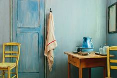 a painting of a blue door in a room with two chairs and a small table