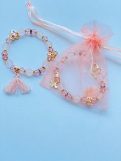 two bracelets with tassels and beads on a light blue background next to a pink organ bag