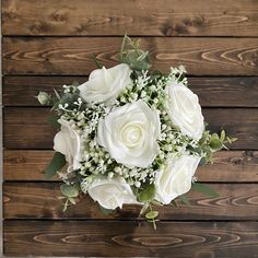 a bouquet of white roses and greenery on a wooden surface with wood planks