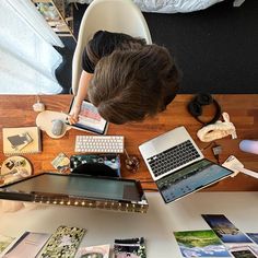 a person sitting at a desk with several laptops and books on it, looking down