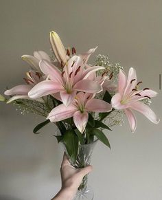 a vase filled with pink flowers on top of a table next to a person's hand