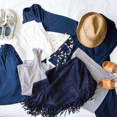 clothes and hats laid out on a bed with white sheets, blue shorts and shoes