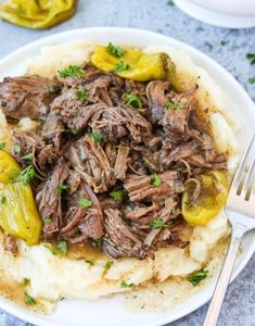 a white plate topped with mashed potatoes covered in beef and peppers next to a fork