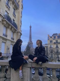 two women sitting on a ledge in front of the eiffel tower