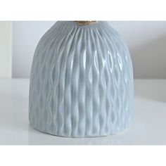 a white vase sitting on top of a table next to a wall with a light blue background