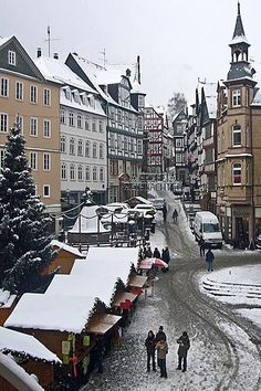 several people walking down a snowy street lined with tall buildings and small shops on either side