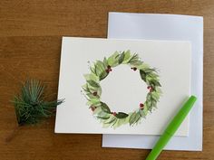 a card with a watercolor painting of a wreath on it and a green marker next to it