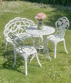 a white table and chairs sitting on top of a grass covered field with flowers in a vase