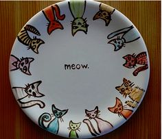 a plate with cats painted on it that says meow in front of a wood background